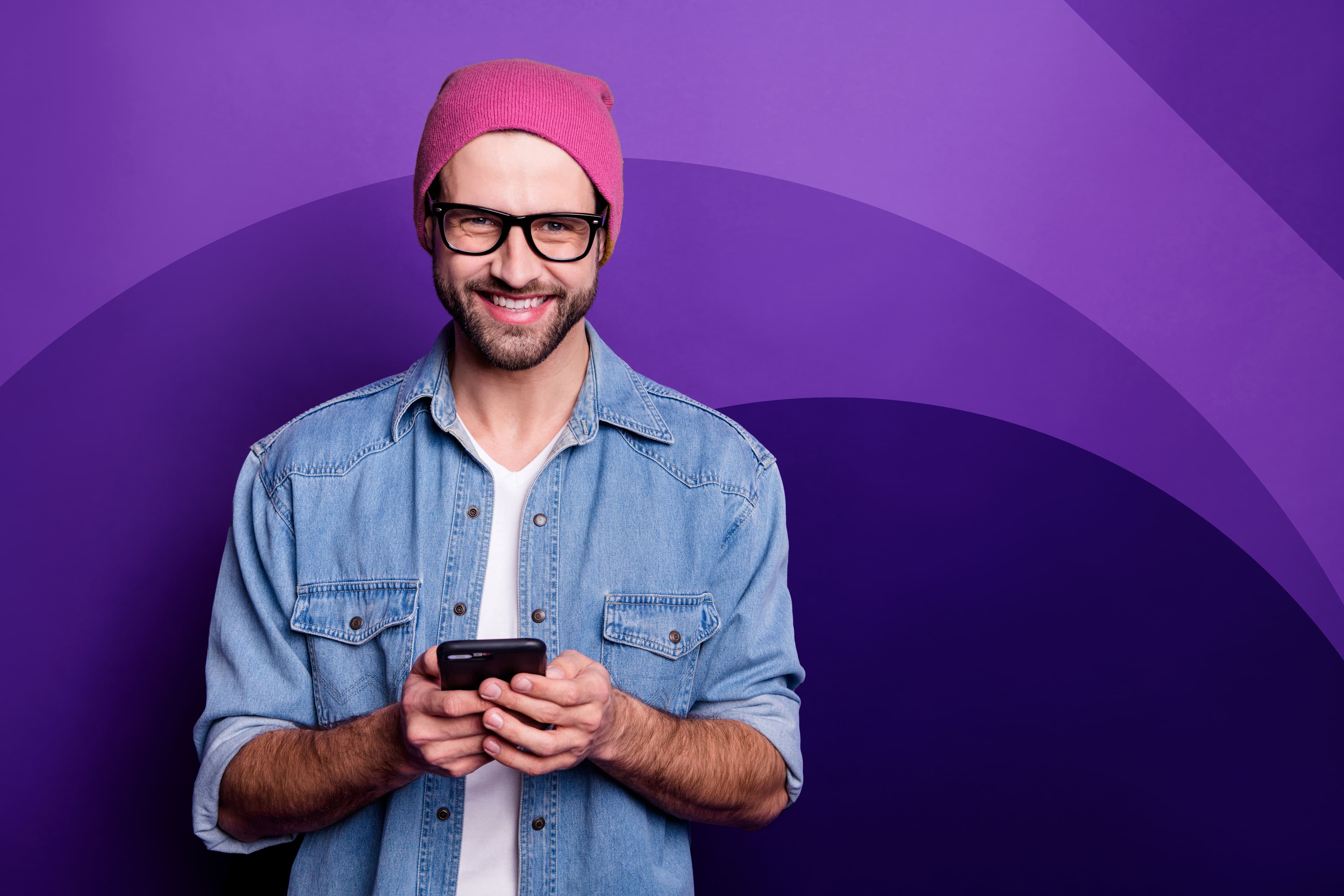 Cool guy holding smartphone using web app casual wearing denim outfit isolated from violet background.